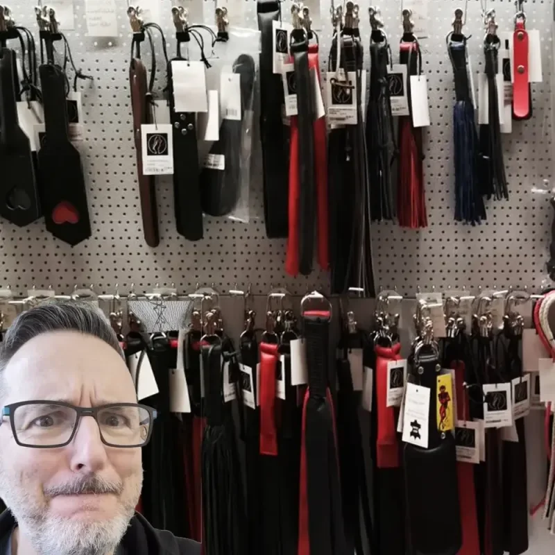 Mann mit Brille vor einer Wand mit aufgehängten Leder- und Baumwollseilen in einem Laden