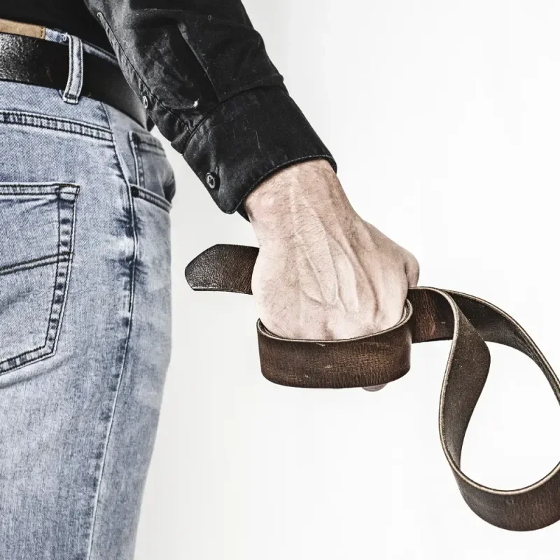 Hand hält einen Ledergürtel neben hellblauer Jeans vor weißem Hintergrund