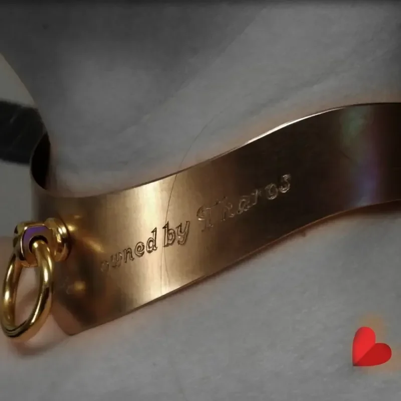 Graviertes Metallband mit Ring auf hellem Stoff, daneben ein rotes Herz-Symbol