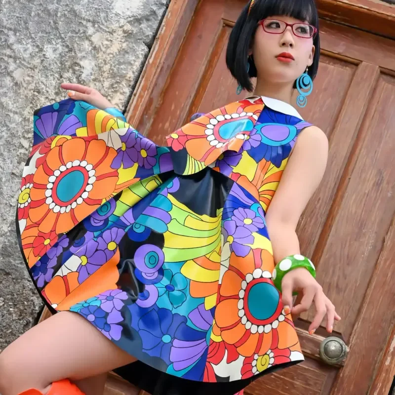 Person in farbenfrohem, floral gemustertem Kleid vor einer Holztür.