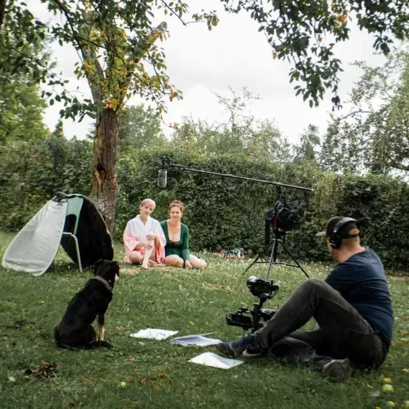 Filmteam dreht ein Interview mit zwei Frauen im Garten, während ein Hund zusieht