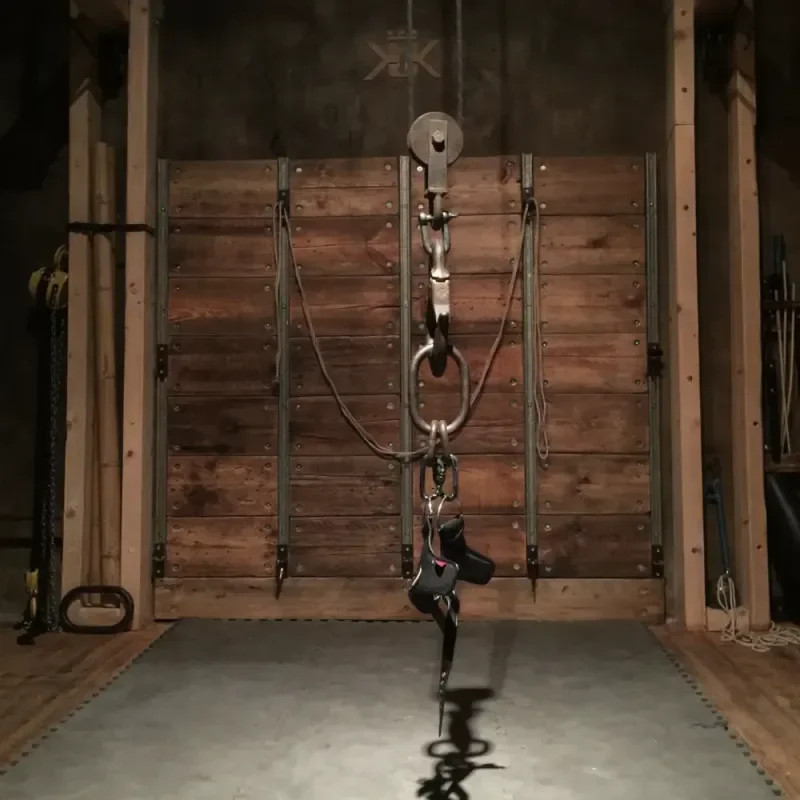 Dunkler BDSM-Spielraum mit Holzwand, Seilzügen, Haken und Aufhängung in der Mitte