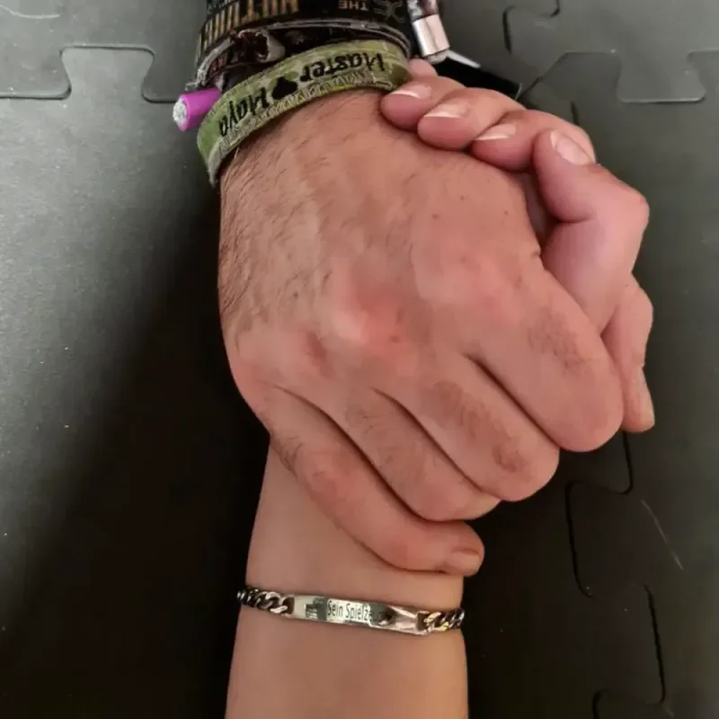 Zwei ineinander verschränkte Hände auf schwarzer Matte, eine mit Armbändern, als Cover der Podcastfolge zu Body-Play
