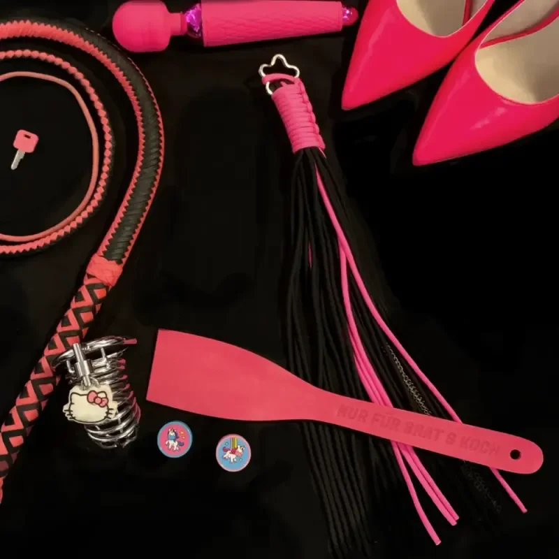 Pinkes BDSM-Zubehör mit Peitschen, Paddel, Vibrator und High Heels auf schwarzem Hintergrund