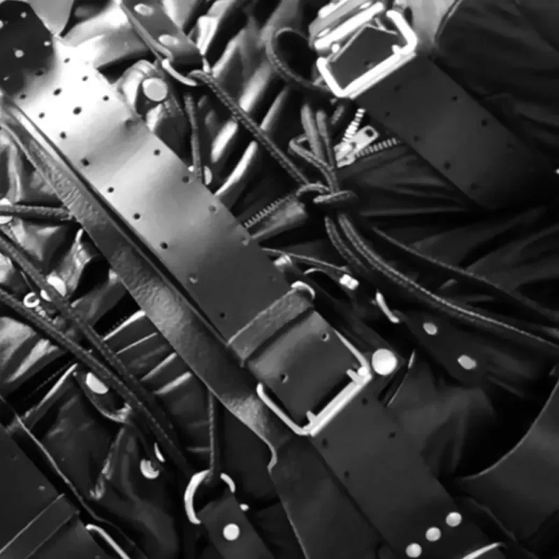 Schwarz-weißes Close-up von schwarzem Leder mit Riemen, Schnallen, Nieten und Schnürungen