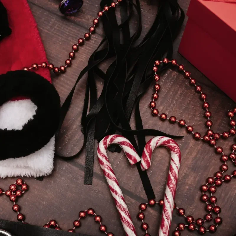 Weihnachtliche Deko mit Zuckerstangen, Perlenketten, roter Mütze und schwarzen Bändern auf dunklem Holz