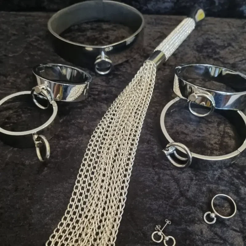 Metallhalsbänder, Handschellen und Kettenpeitsche auf schwarzem Stoff