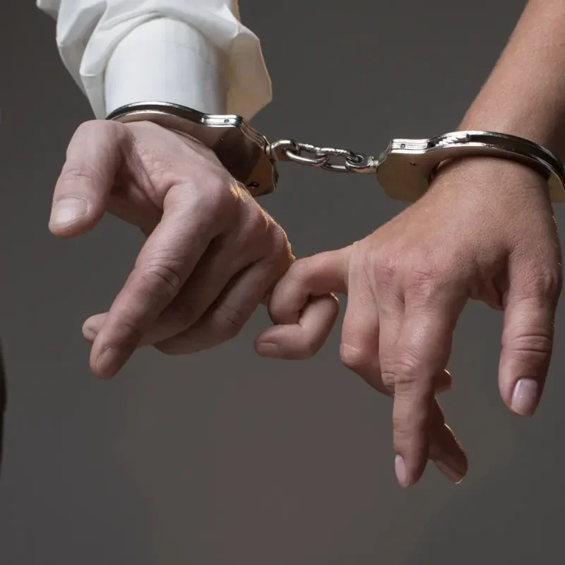 Zwei Hände sind mit Handschellen aneinandergekettet vor dunklem Hintergrund