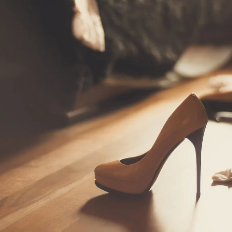 Eleganter High Heel auf einem Holzboden im warmen Licht.