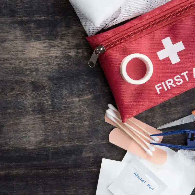 Rote Erste-Hilfe-Tasche mit Verbandsmaterial und Schere auf dunklem Holzuntergrund