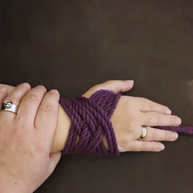 Hände mit violettem Seil gefesselt auf dunklem Hintergrund
