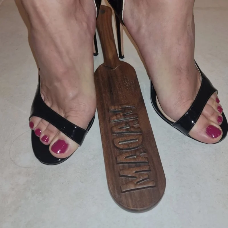 Füße in schwarzen Sandalen stehen auf einem Holzpaddel mit der Aufschrift LADY.
