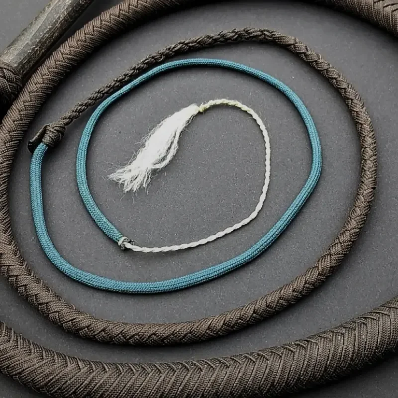 Geflochtene Bullwhip mit blauem Griff und weißem Ende liegt spiralförmig auf dunklem Untergrund