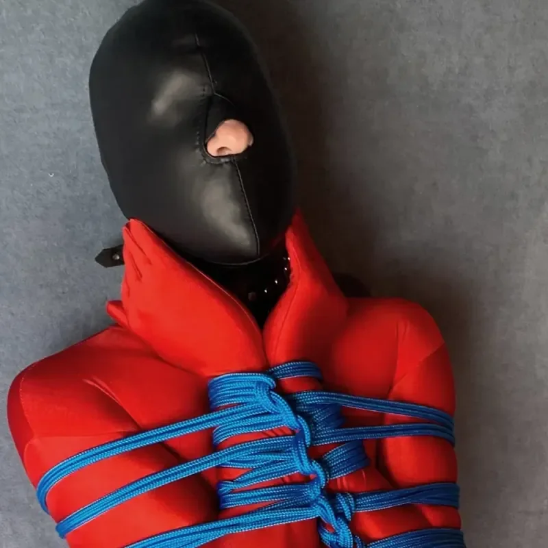 Person in rotem Outfit mit schwarzer Maske und blauer Seilfesselung vor grauem Hintergrund