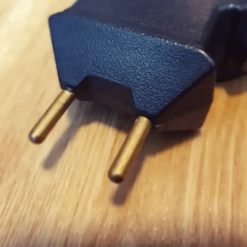 Schwarzer Eurostecker mit zwei Metallstiften auf hellem Holztisch