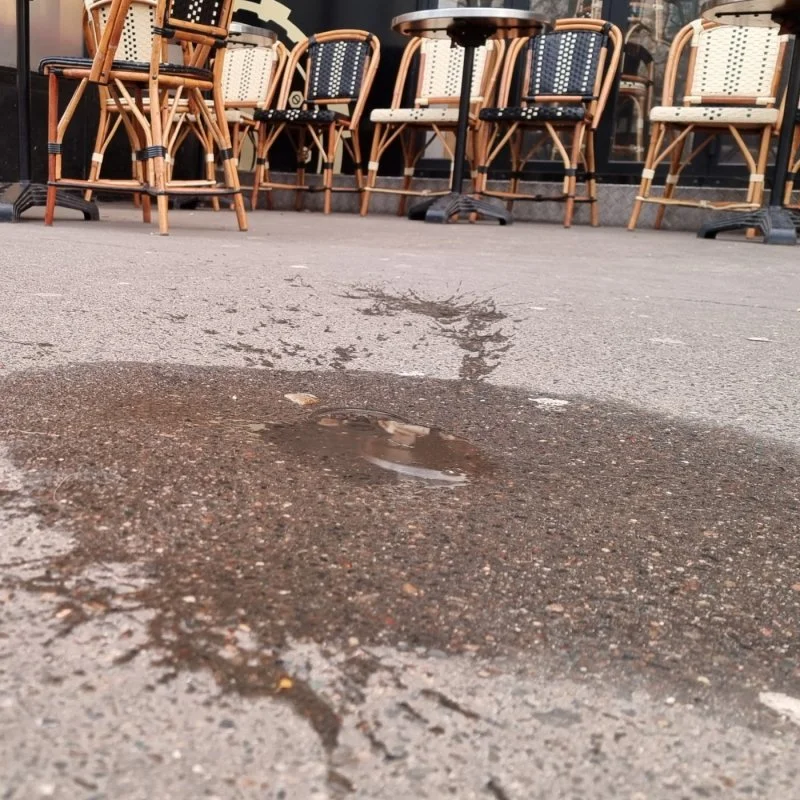 Leere Caféterrasse mit Stühlen und einer Pfütze auf dem Boden aus niedriger Perspektive