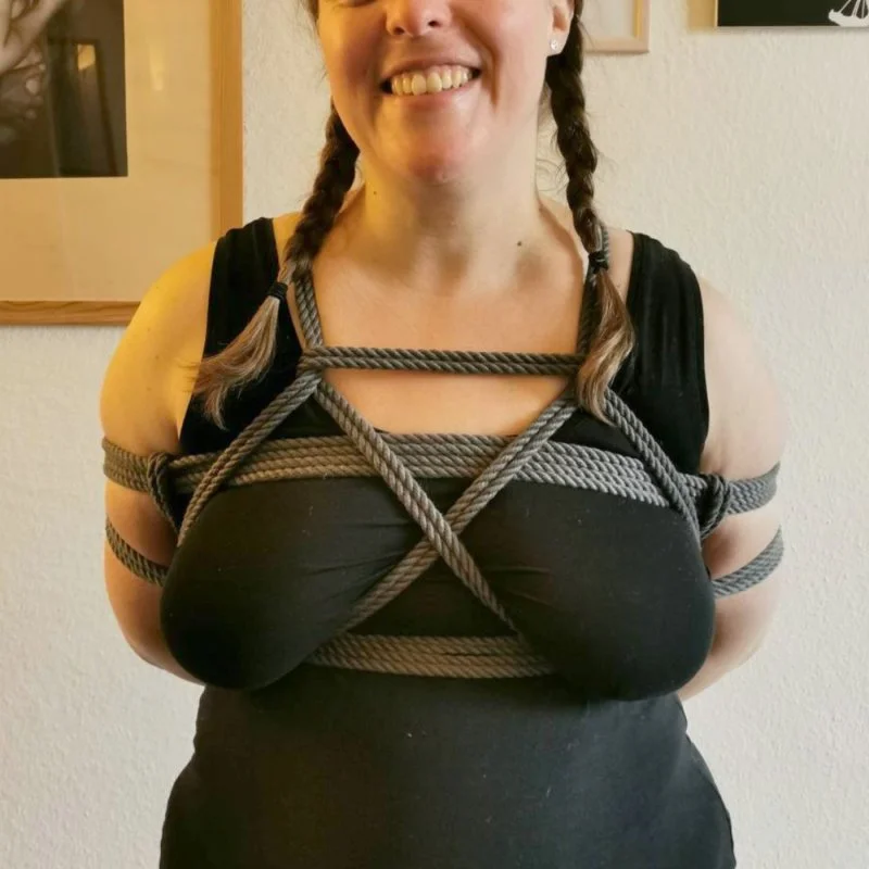 Lächelnde Frau mit gefesseltem Oberkörper vor hellem Hintergrund