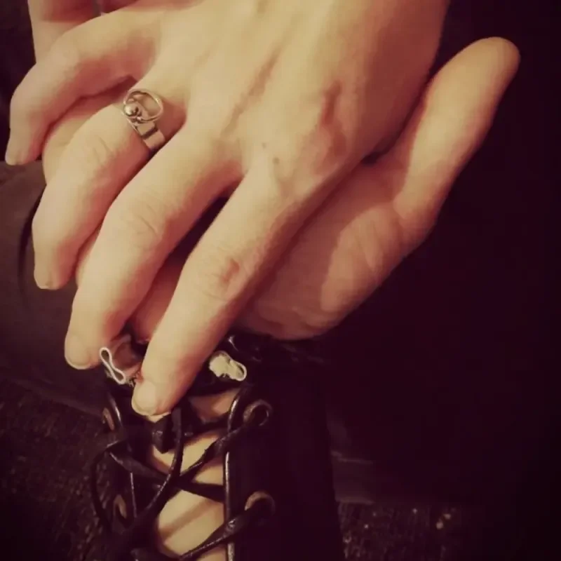 Hand mit Ring greift an die Schnürung eines schwarzen Stiefels vor dunklem Hintergrund