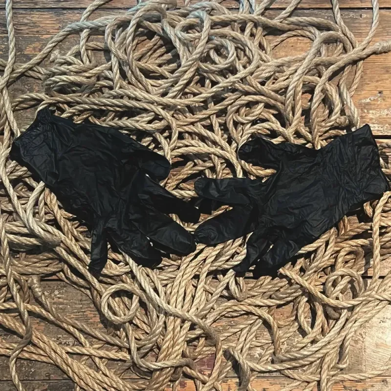 Verknotete Seile und schwarze Handschuhe auf einem Holzboden