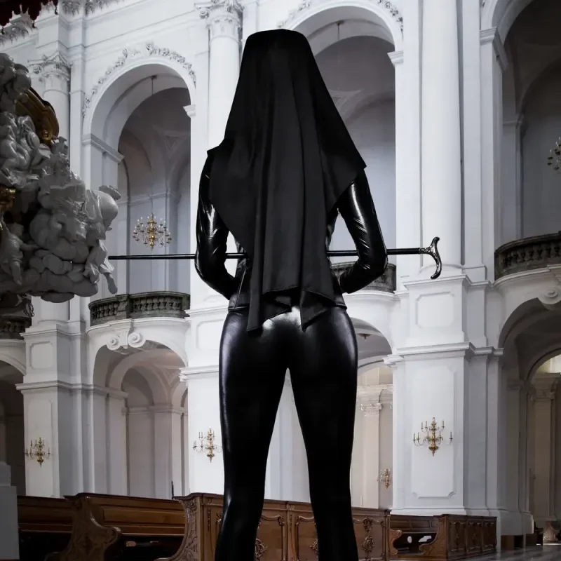 Person in schwarzem Latexanzug und Schleier steht in einer prunkvollen Kirche