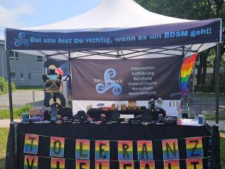 Informationsstand von SM Lübeck e.V. mit BDSM- und Toleranz-Bannern auf einer Veranstaltung