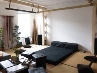 Heller Wohnraum mit schwarzem Futon, Pflanzen, niedrigen Tischen und Holzgestell an Wand und Decke.