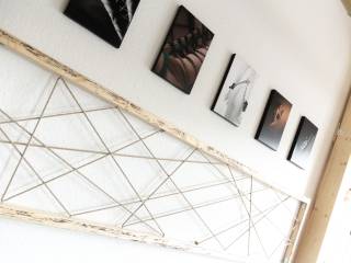 Schräg aufgenommene Wand mit kleinen gerahmten Fotos und einer großen geometrischen Fadenkonstruktion.