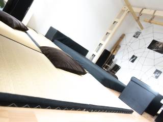 Schräg fotografierter Wohnraum mit hellem Sofa, dunklen Kissen, Sessel und geometrischer Wanddekoration.