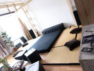 Helles Wohnzimmer mit Tatami-Matten, schwarzem Sofa, Pflanzen, Kissen und niedrigen Tischen.