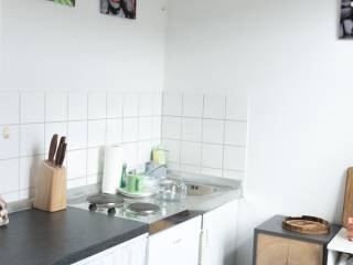 Kleine helle Küche mit Spüle, Herdplatten, weißen Fliesen, Wandbildern und schmalem Regal.