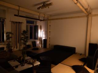 Gedämpft beleuchteter Wohnraum mit Sofa, Tisch, Pflanzen und freier Wandfläche.